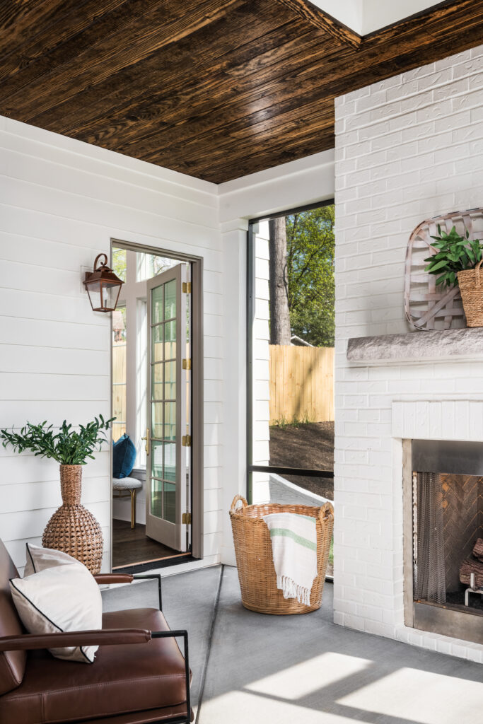 Luxury screened porch with white brick fireplace, stained wood ceiling, and outdoor living area.