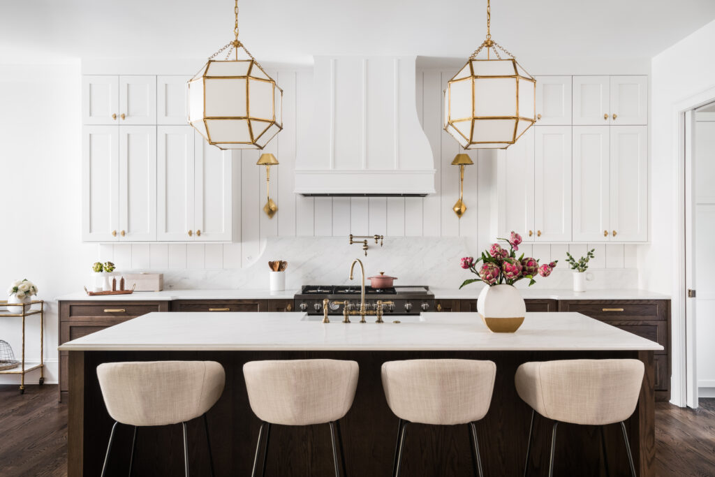 Luxury custom kitchen in Charlotte, NC with white cabinetry, dark wood island, natural stone countertops, and brass lighting.