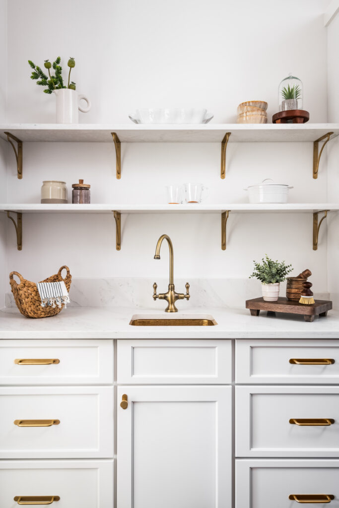 Custom butler's pantry with white cabinetry, open shelving, marble-look countertops, and brass fixtures.