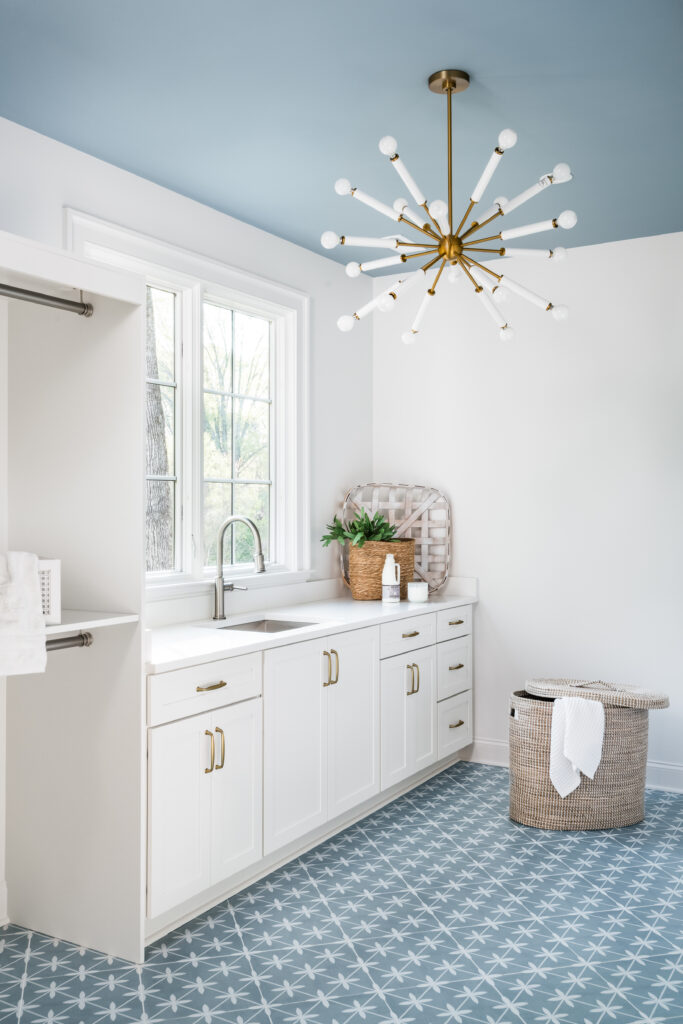 Custom laundry room with blue ceiling and patterned tile, white cabinetry, champagne bronze hardware, and statement lighting.