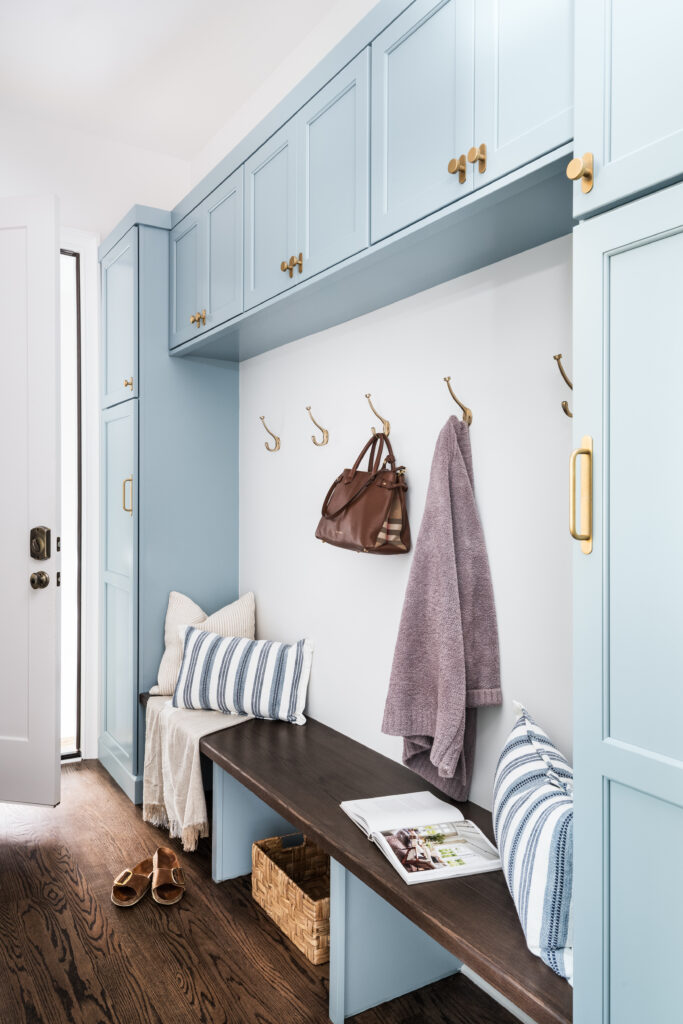 Custom drop zone with blue cabinetry, stained bench seating, ample storage, and brass hardware.