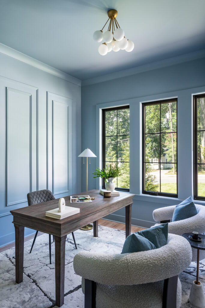 Custom luxury home office with blue walls, decorative millwork, designer lighting, and abundant natural light.
