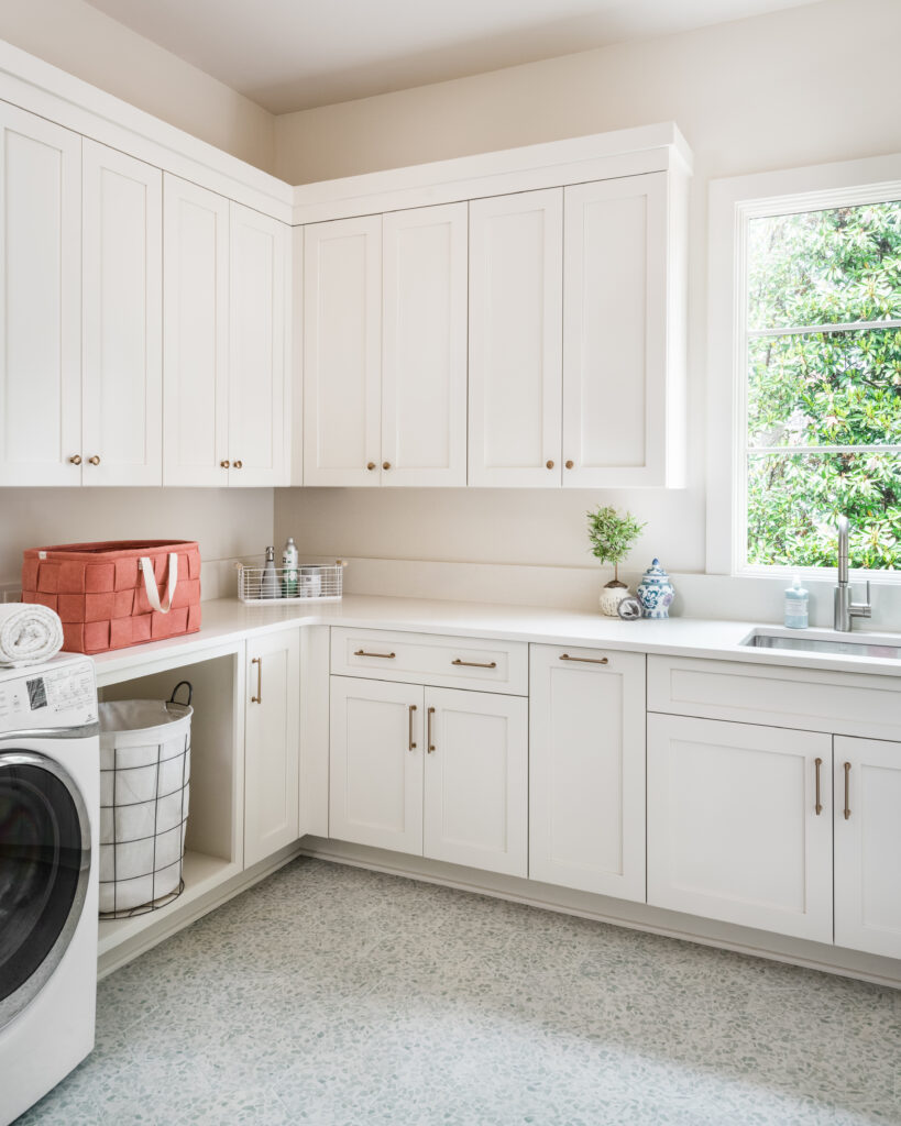 Custom laundry room in luxury Charlotte, NC home with white cabinetry, abundant storage and counter space, natural light, and tile flooring.