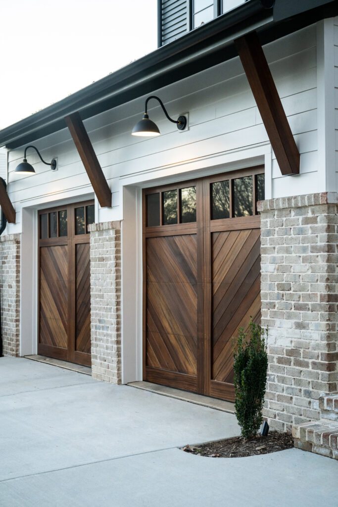 Luxury custom home exterior with wood garage doors, brick detailing, and designer exterior lighting.